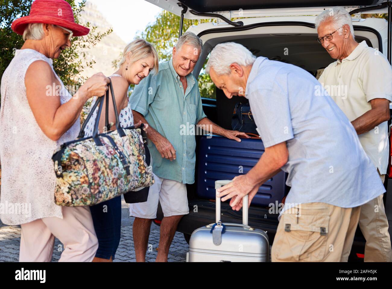 Gruppo di amici Senior di carico dei bagagli nel tronco della vettura in procinto di partire per le vacanze Foto Stock