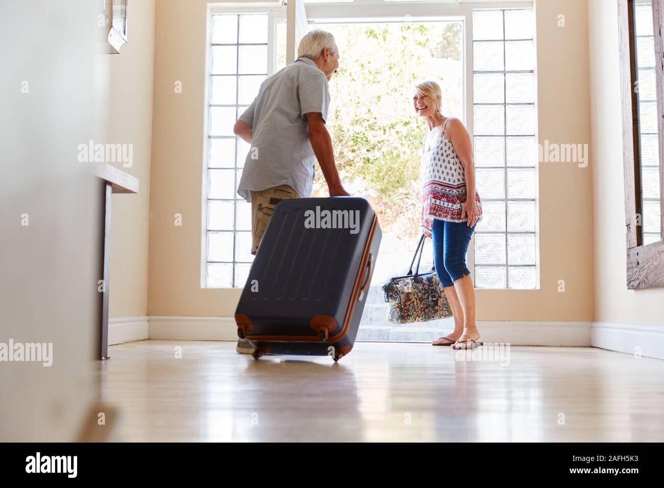 Coppia senior in piedi dalla Porta anteriore con la valigia in procinto di partire per le vacanze Foto Stock