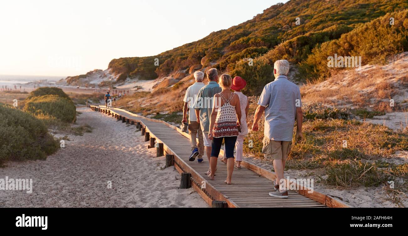 Gruppo di amici Senior camminare lungo la passeggiata a mare in spiaggia in estate vacanze di gruppo Foto Stock