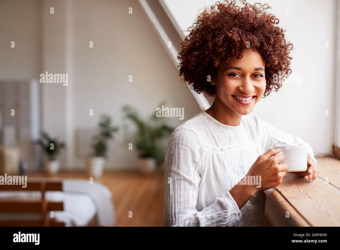 Ritratto di giovane donna in Relax Appartamento Loft guardando fuori della finestra con bevanda calda Foto Stock