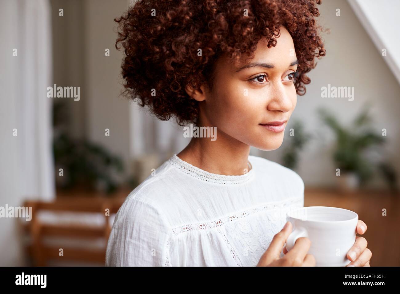 Giovane donna rilassante in appartamento loft con bevanda calda Foto Stock