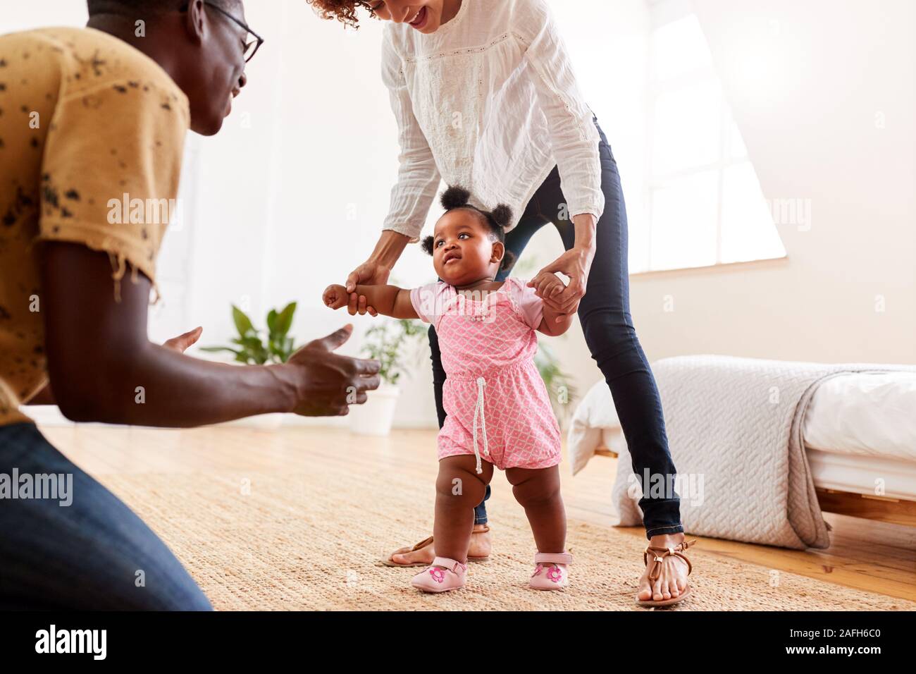 I genitori a casa incoraggiando la nostra bambina di prendere i primi passi Foto Stock