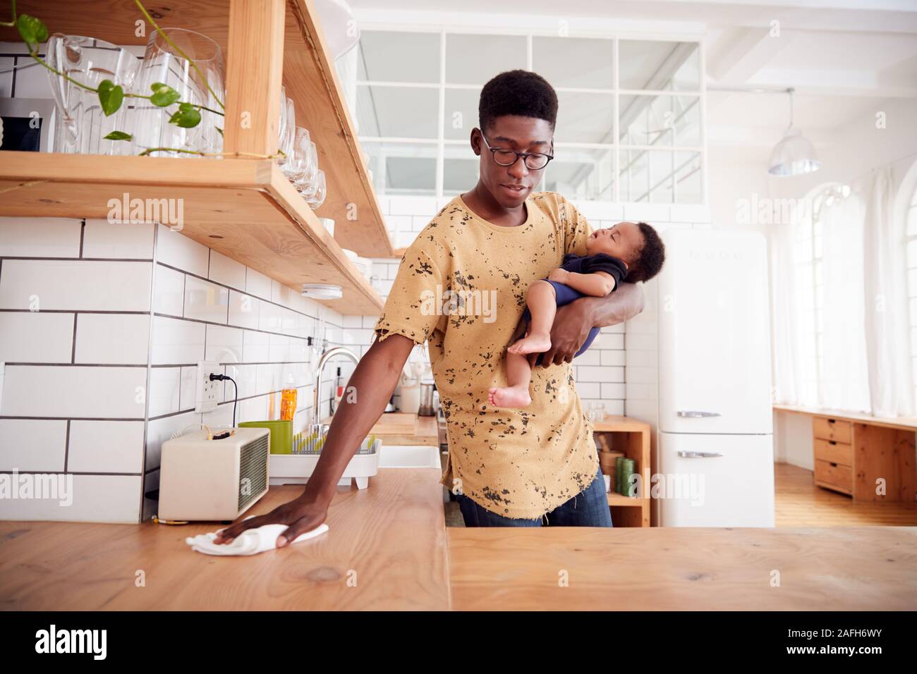 Multitasking Padre tiene il bambino dorme figlio e pulisce in cucina Foto Stock
