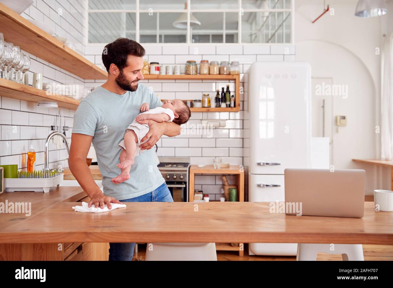 Multitasking Padre tiene il bambino dorme figlio e pulisce in cucina Foto Stock