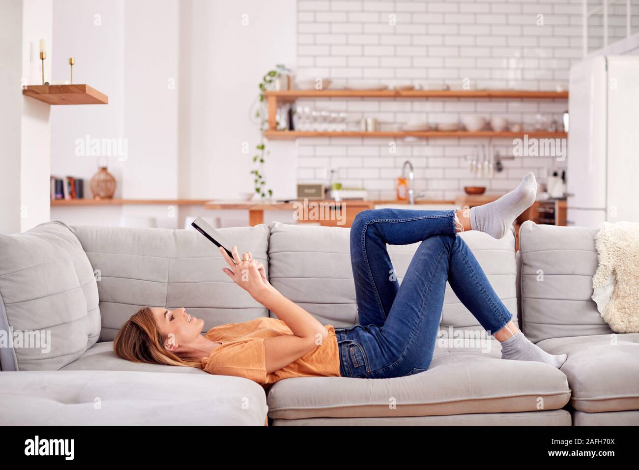 Donna rilassante sdraiato sul divano di casa guardando a tavoletta digitale Foto Stock