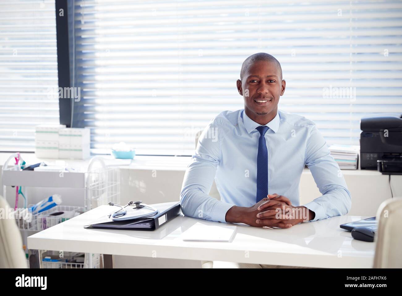 Ritratto di sorridente medico maschile seduto alla scrivania in ufficio Foto Stock