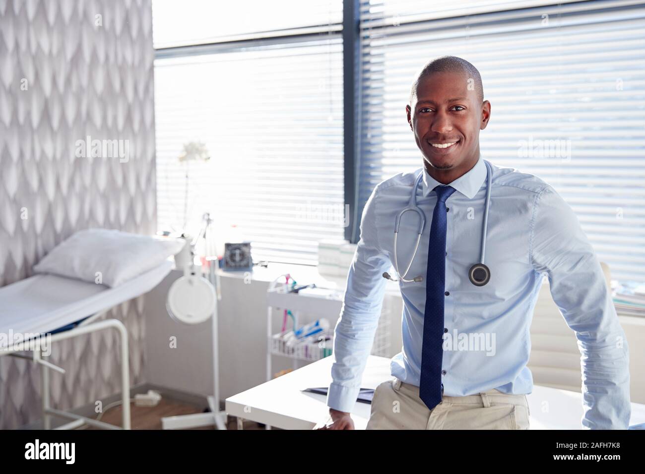 Ritratto di sorridente medico maschio con uno stetoscopio in piedi da scrivania in ufficio Foto Stock