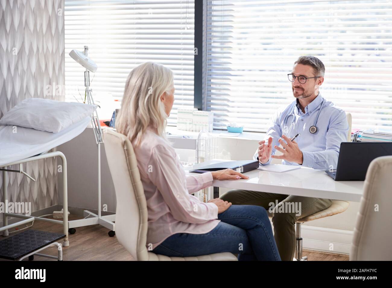 Femmina matura paziente in consultazione con il medico seduto alla scrivania in ufficio Foto Stock