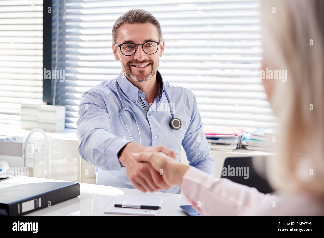 Paziente di sesso femminile si stringono la mano con il medico seduto alla scrivania in ufficio Foto Stock