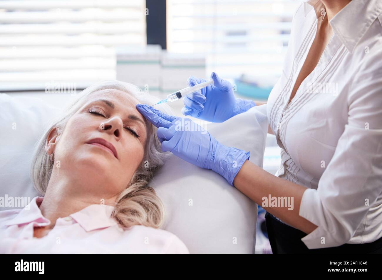 Estetista dando femmina matura paziente iniezione di Botox in fronte Foto Stock