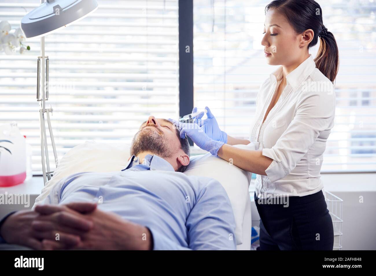 Estetista femmina dando maschio maturo paziente iniezione di Botox in fronte Foto Stock