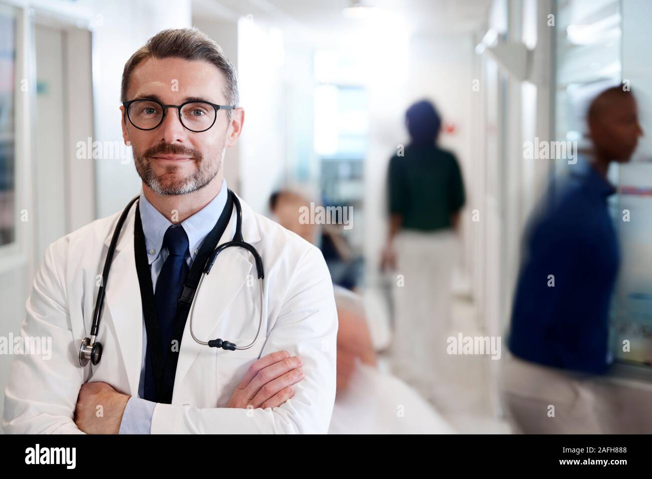 Ritratto di maschio maturo medico indossa mantello bianco con uno stetoscopio in ospedale occupato corridoio Foto Stock