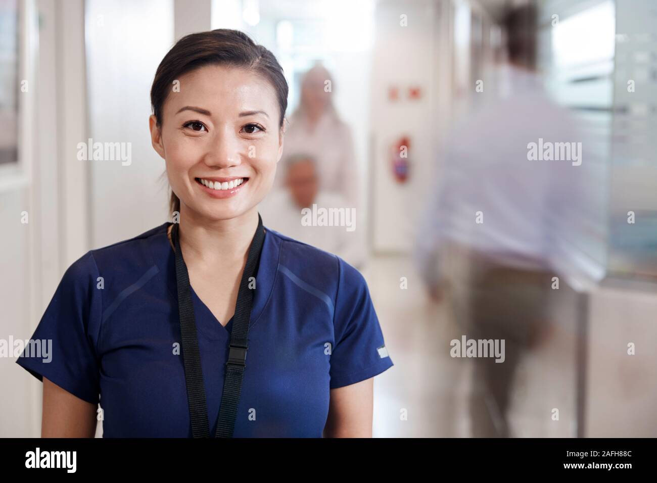 Ritratto Di Donna sorridente infermiera indossando Scrubs in ospedale occupato corridoio Foto Stock