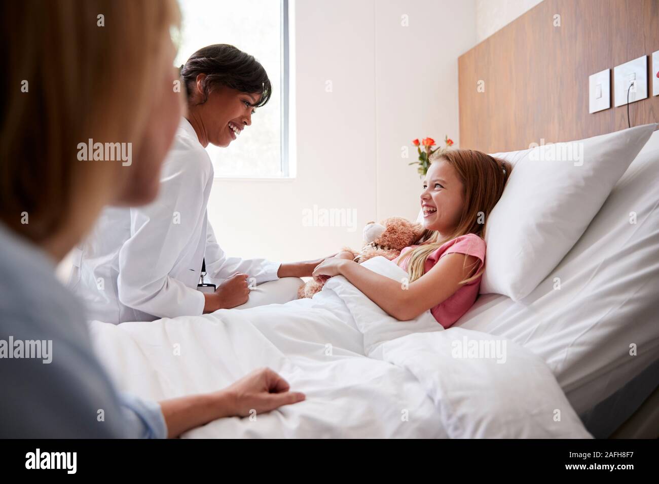 Medico donna in visita a madre e figlia che giace nel letto di ospedale Foto Stock