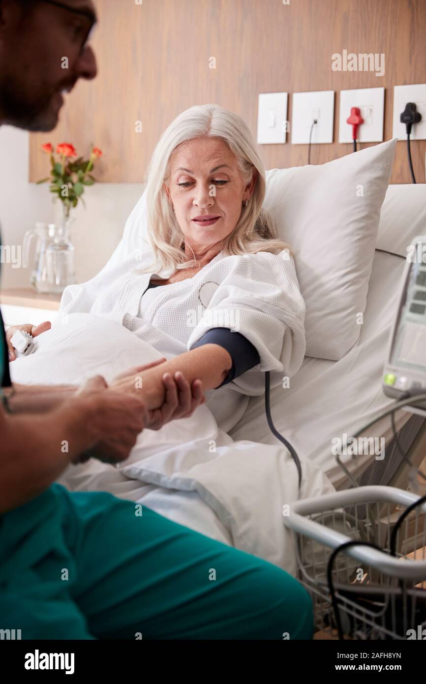 Infermiere maschio presa femmina matura pazienti la pressione del sangue nel letto di ospedale con macchina automatica Foto Stock