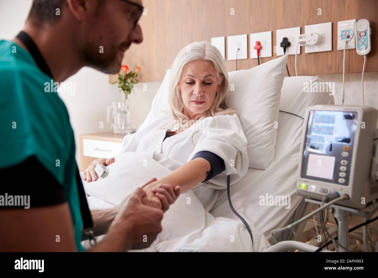 Infermiere maschio presa femmina matura pazienti la pressione del sangue nel letto di ospedale con macchina automatica Foto Stock