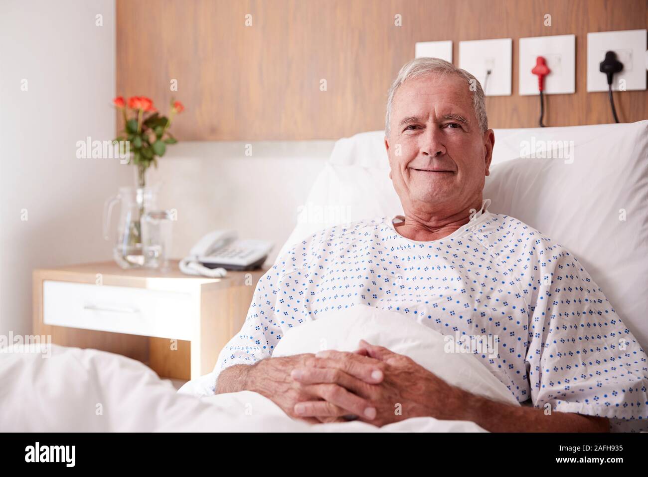 Ritratto di Senior maschili paziente sdraiato nel letto di ospedale sorridente in telecamera Foto Stock