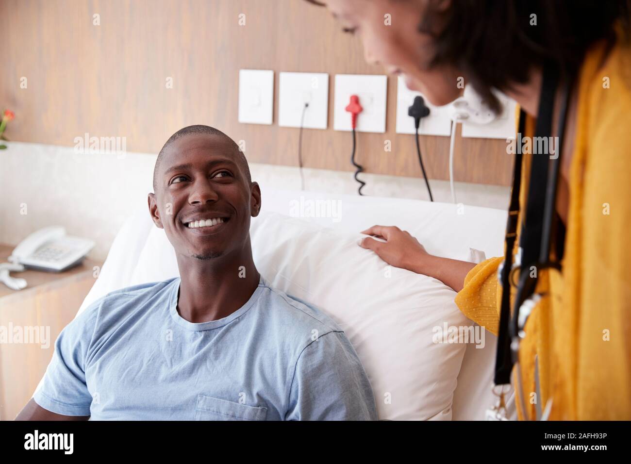 Medico con tavoletta digitale visitando e parlando con il paziente di sesso maschile nel letto di ospedale Foto Stock
