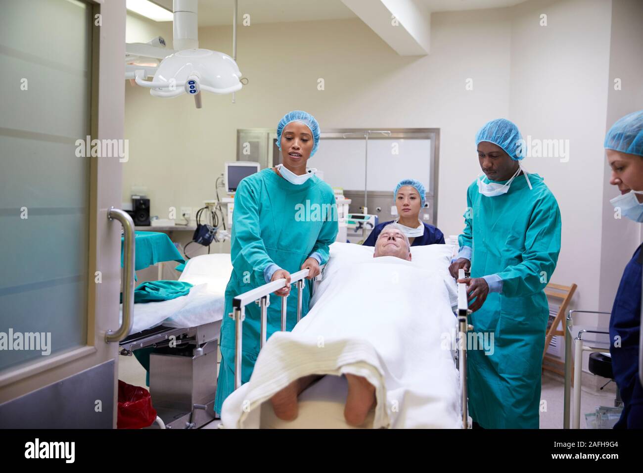 Il team chirurgico Wheeling Senior paziente di sesso maschile di ospedale teatro operativo Foto Stock
