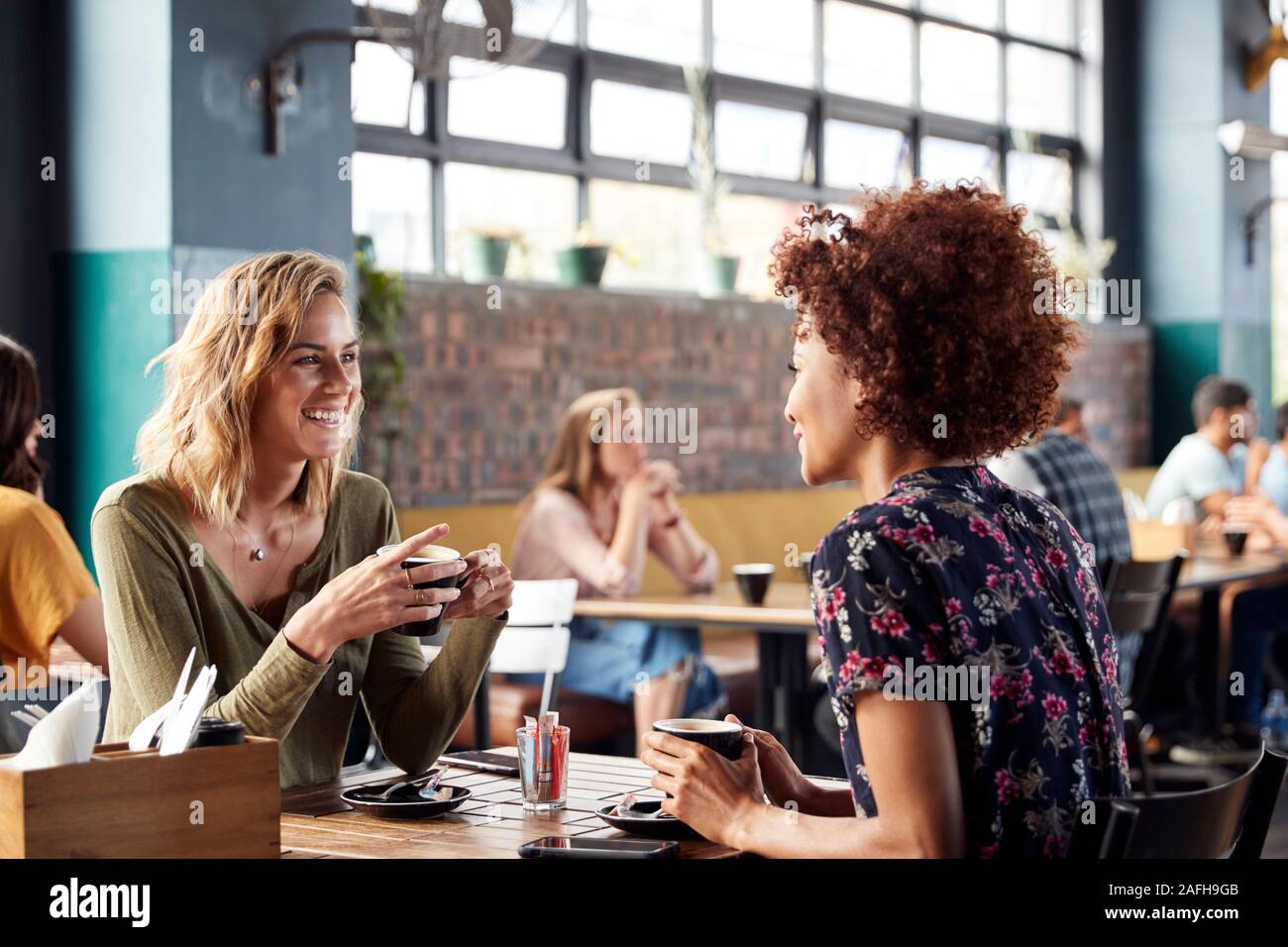 Due amiche incontro sedersi a tavola in un Coffee Shop e parlare Foto Stock