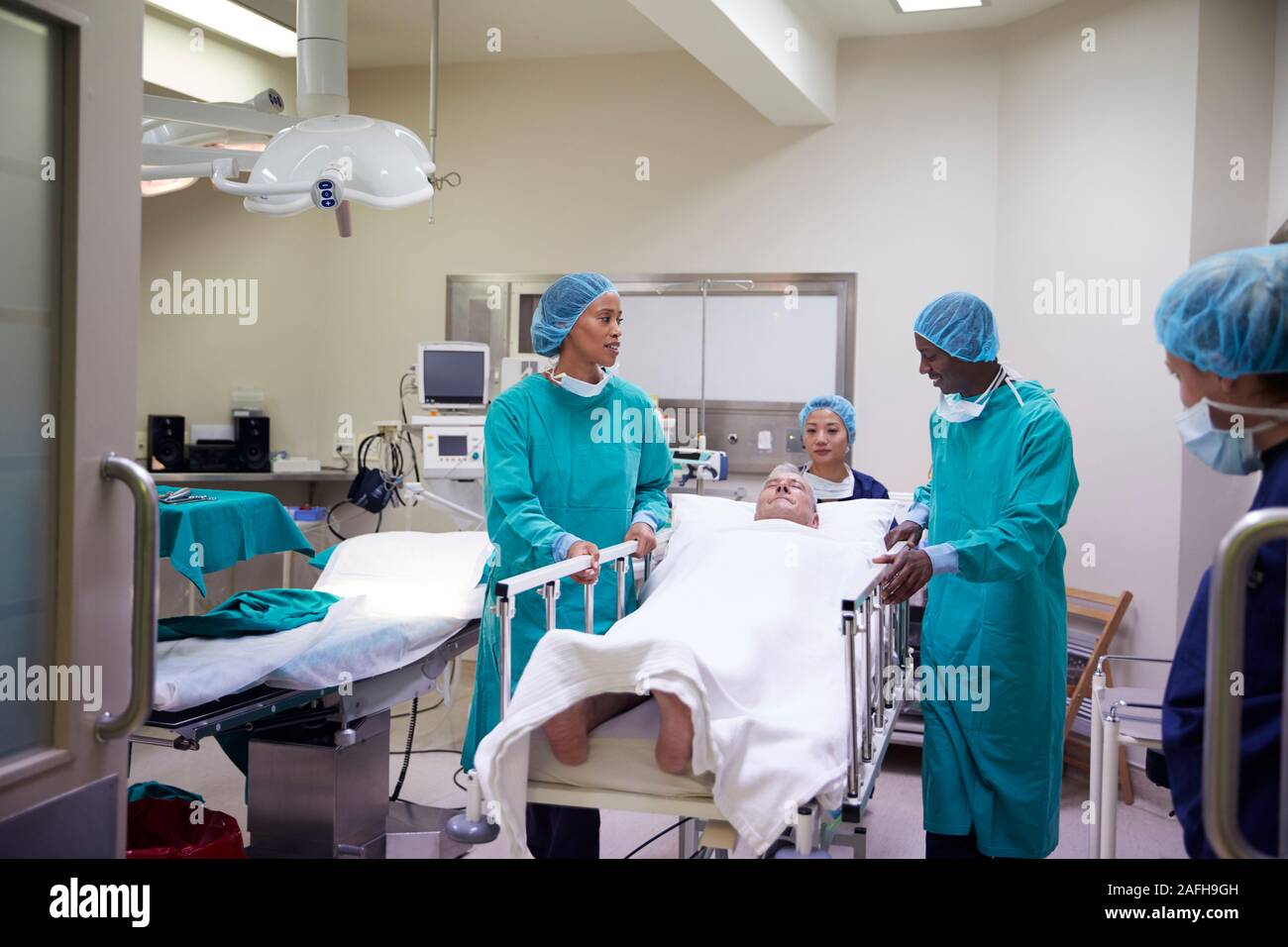 Il team chirurgico Wheeling Senior paziente di sesso maschile di ospedale teatro operativo Foto Stock