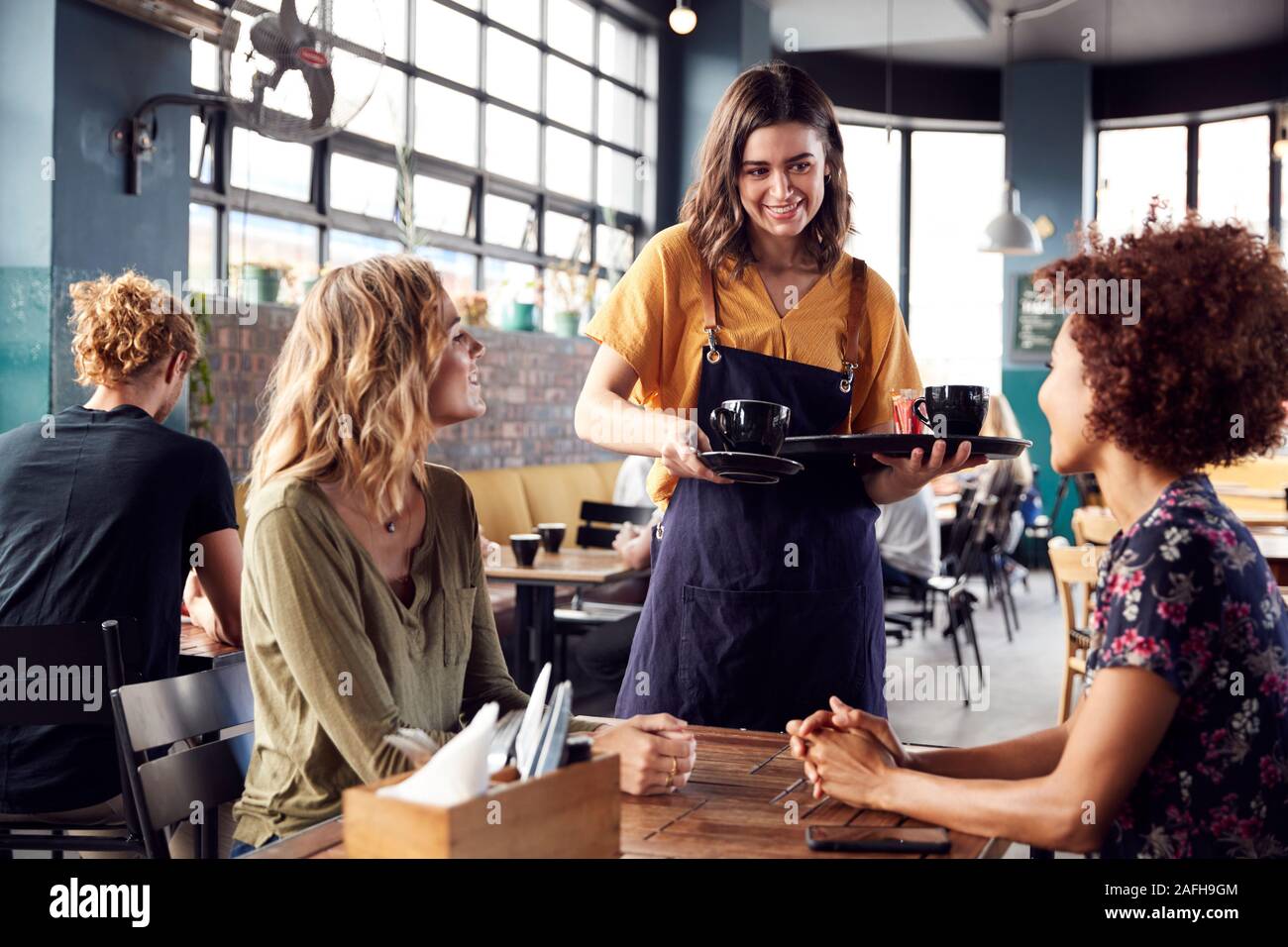 Due amiche seduta a tavola in Coffee Shop essendo servito dalla cameriera Foto Stock