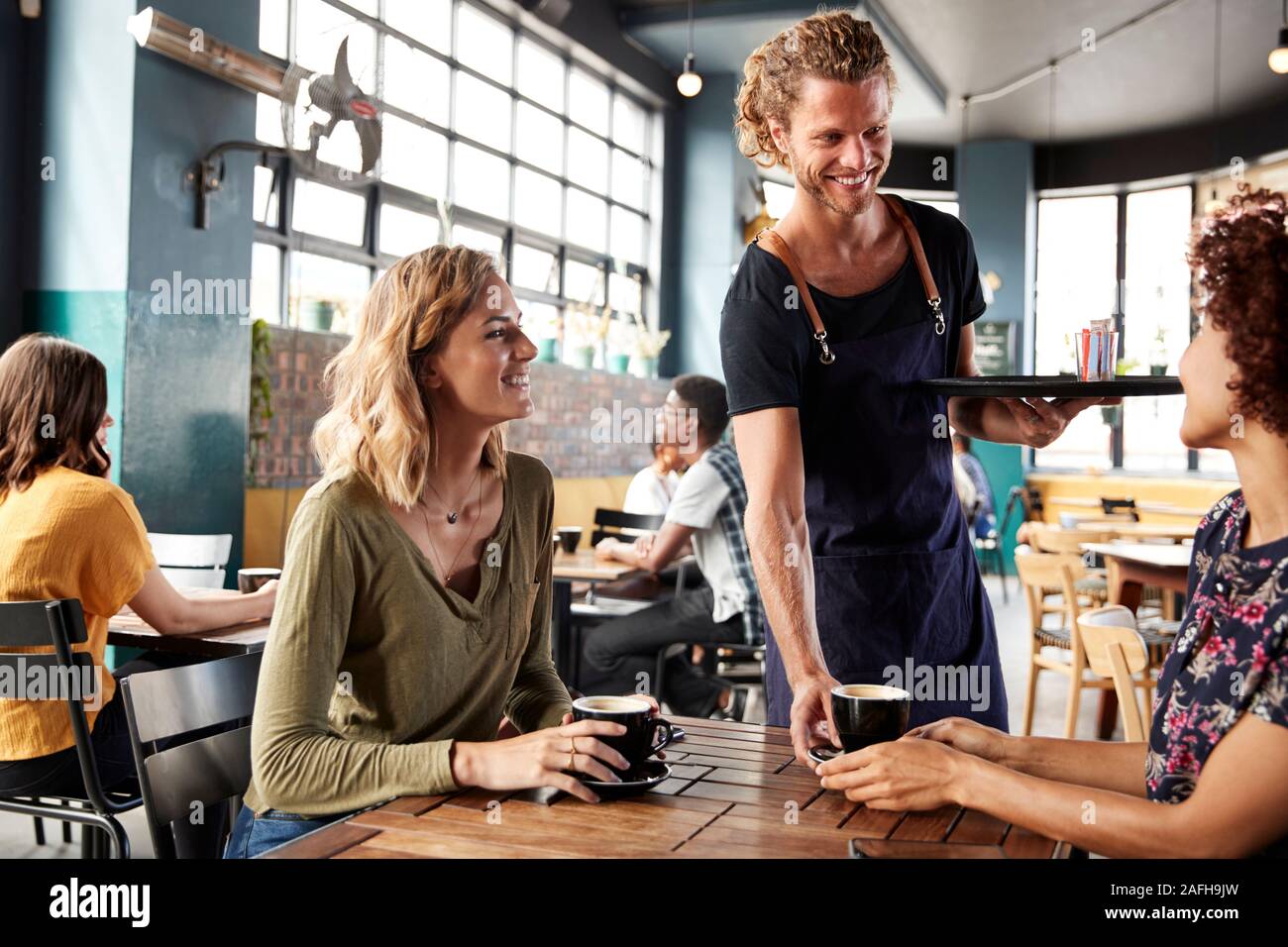 Due amiche seduta a tavola in Coffee Shop servita da un cameriere Foto Stock