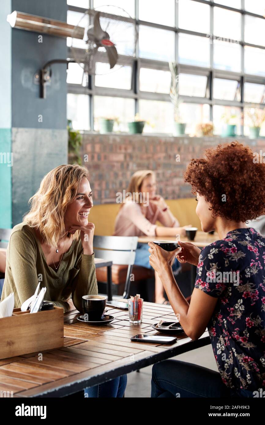 Due amiche incontro sedersi a tavola in un Coffee Shop e parlare Foto Stock