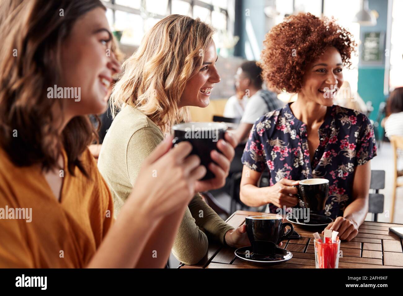 Tre giovani femmine riunione amici siedono al tavolo in un Coffee Shop e parlare Foto Stock