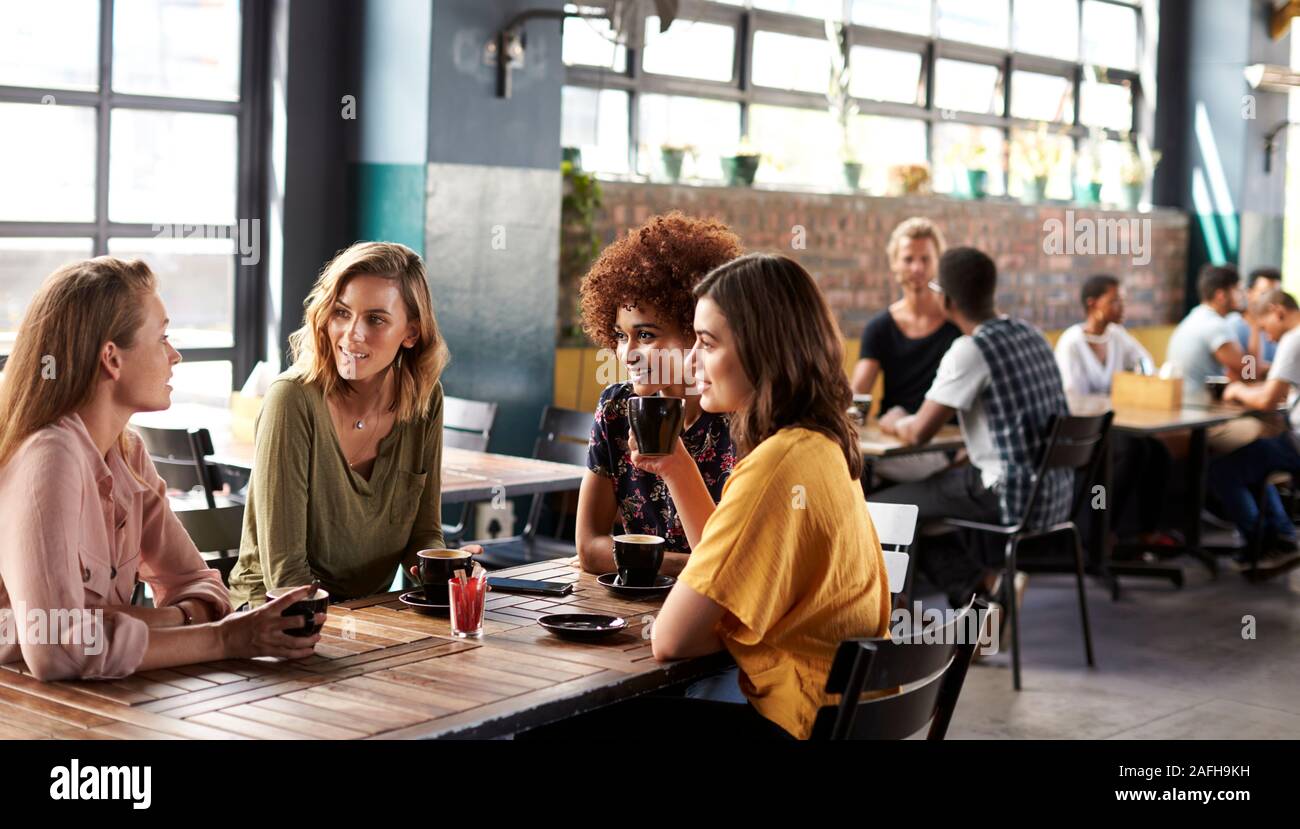 Quattro giovani donne riunione amici siedono al tavolo in un Coffee Shop e parlare Foto Stock