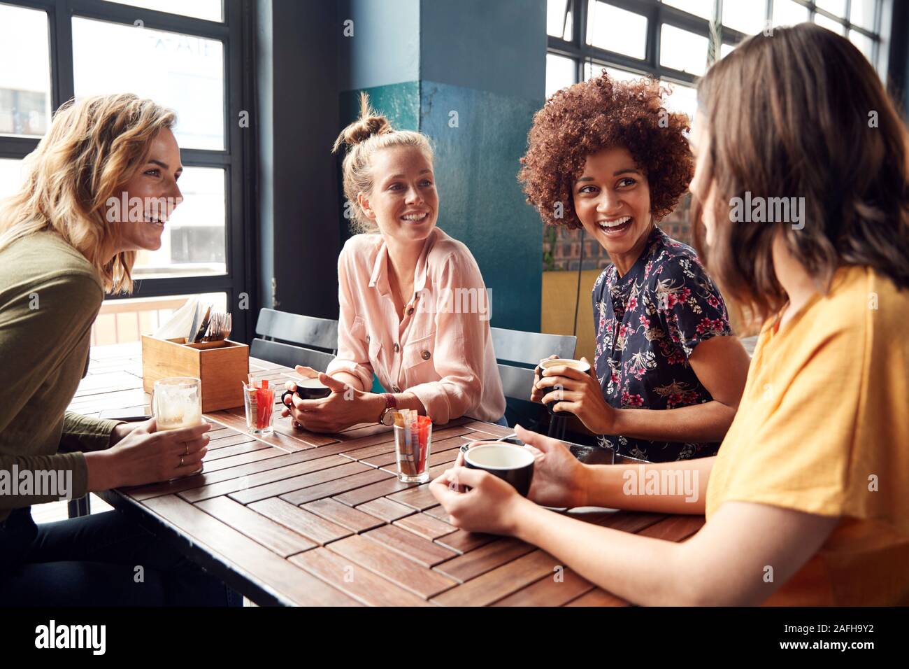 Quattro giovani donne riunione amici siedono al tavolo in un Coffee Shop e parlare Foto Stock