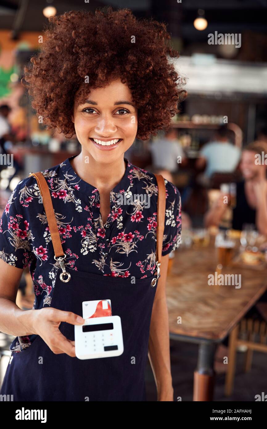 Ritratto di cameriera tenendo il pagamento con carta di credito in terminale occupato Bar Ristorante Foto Stock