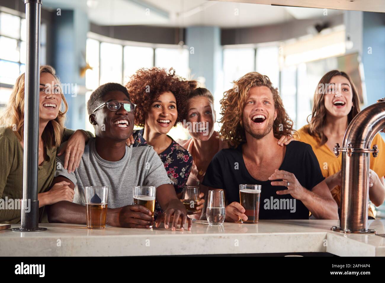 Gruppo di maschio e femmina celebra gli amici mentre si guarda la partita sullo schermo in Sports Bar Foto Stock