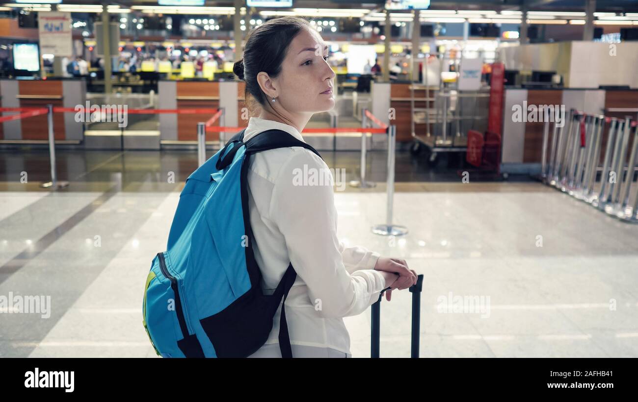 Giovane donna viaggiatori con zaino e valigia in airport terminal, close-up. Lei è in piedi e si guarda intorno, vista posteriore. Foto Stock