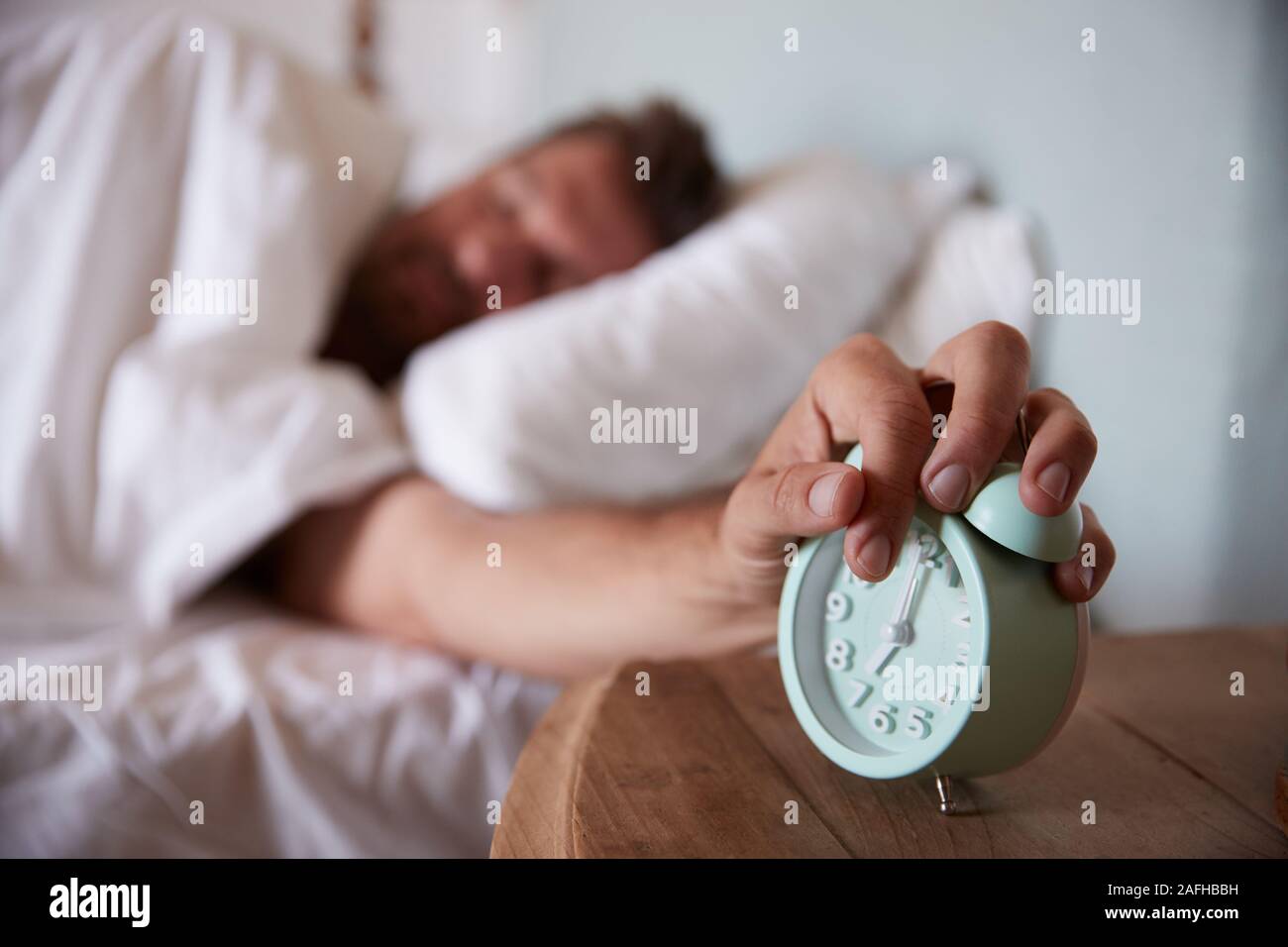 Metà uomo adulto dorme nel letto, raggiungendo le sveglia sul comodino in primo piano Foto Stock