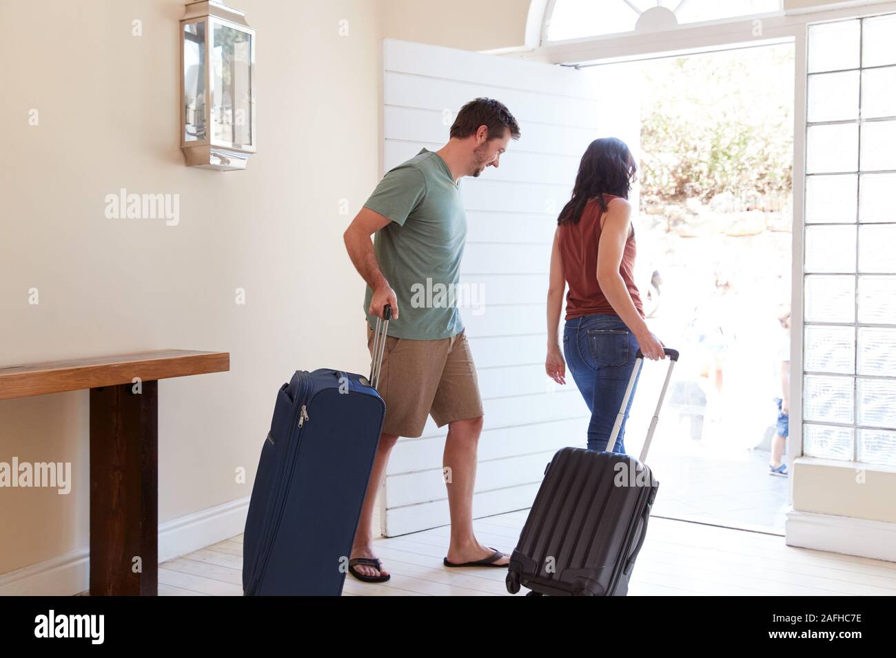 Metà bianco adulto giovane alla loro porta anteriore di uscire di casa con i bagagli per andare in vacanza a piena lunghezza Foto Stock