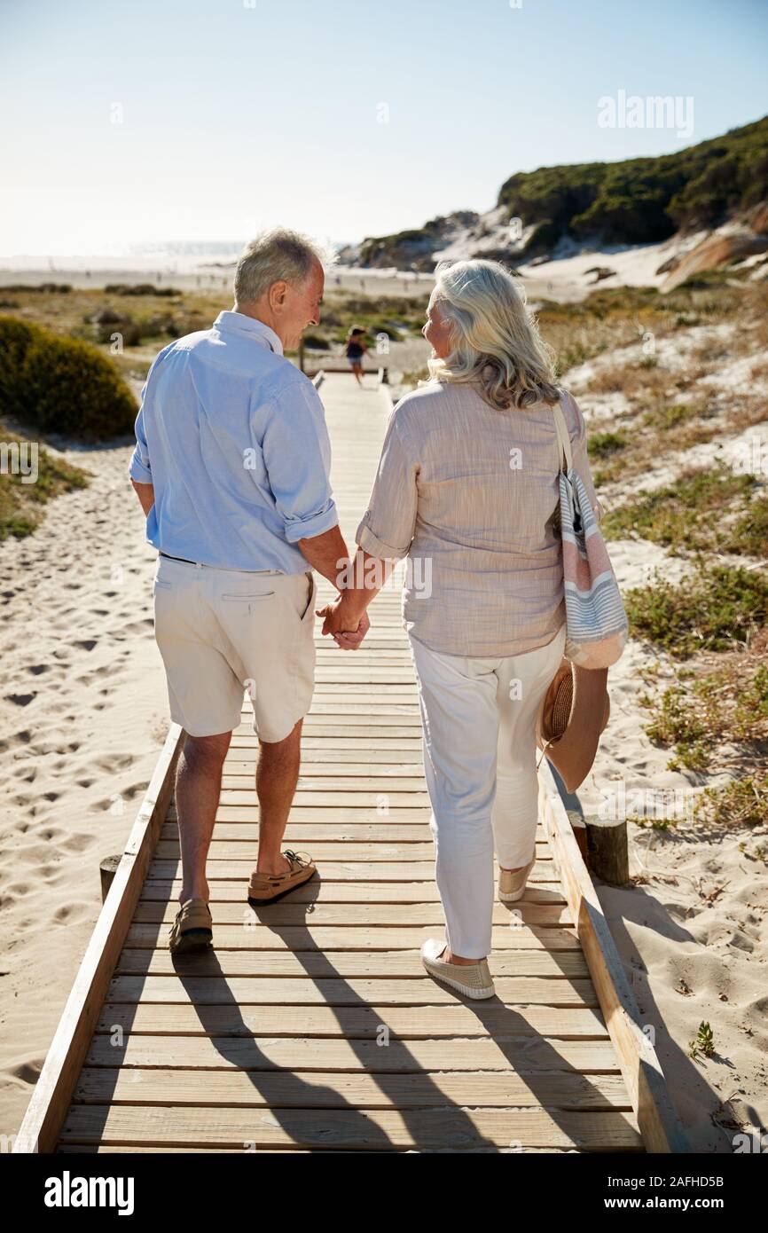 Senior bianco giovane camminare lungo la passeggiata a mare di legno su una spiaggia tenendo le mani a piena lunghezza e vista posteriore Foto Stock