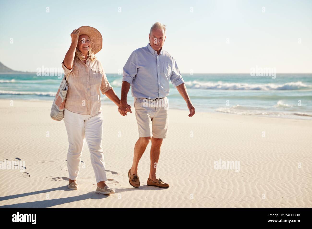 Senior bianco giovane a camminare su una spiaggia insieme tenendo le mani a piena lunghezza e chiudere fino Foto Stock