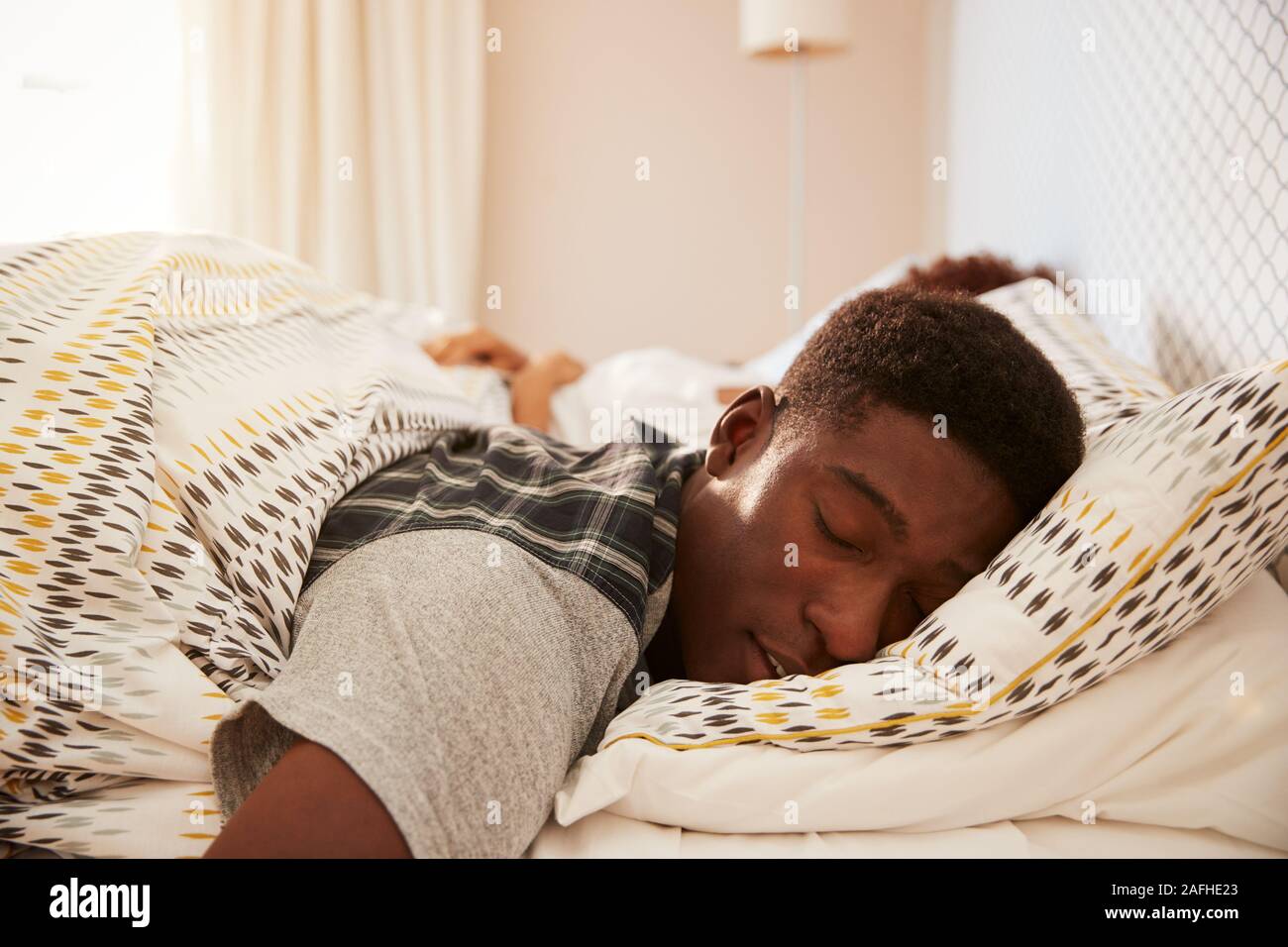 Giovane americano africano uomo disteso addormentato nel letto la mattina, partner in background, la messa a fuoco su oggetti in primo piano Foto Stock
