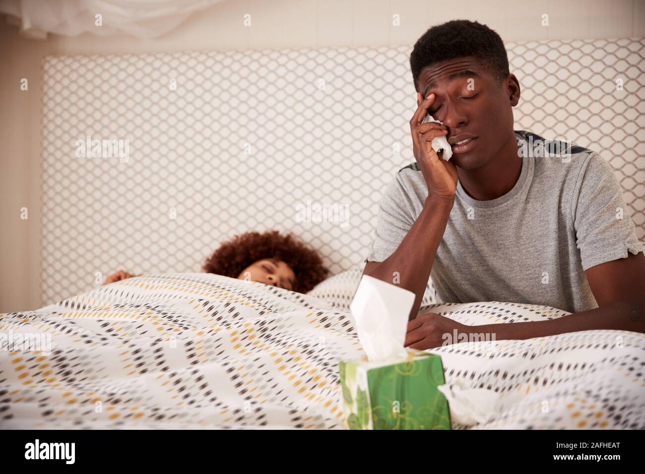 La millenaria African American uomo a letto malato, seduti mentre il partner dorme accanto a lui, close up Foto Stock