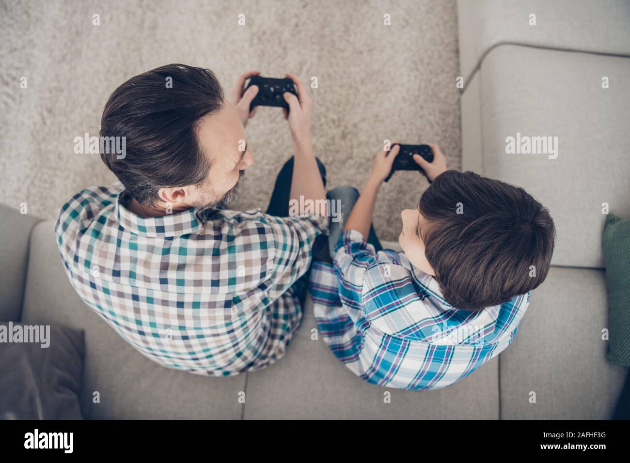 Parte superiore al di sopra ad alto angolo di visione verticale di due belle attraenti ragazzi papà e pre-teen Figlio seduto sul divano godendo la riproduzione del video game pad di ricambio di spesa Foto Stock