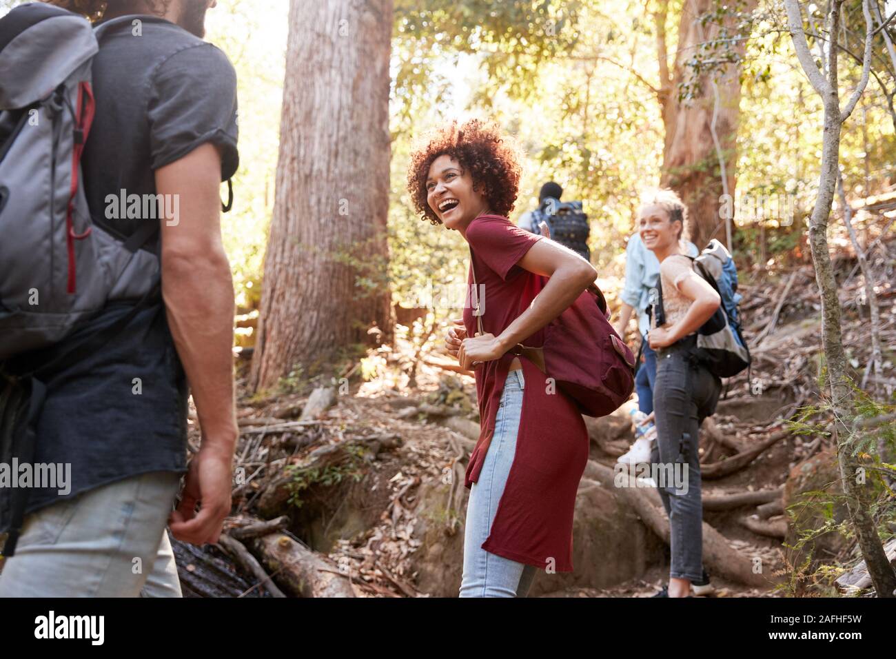 Millennial escursionismo su un sentiero forestale girando intorno a guardare indietro a amici, tre quarti di lunghezza Foto Stock