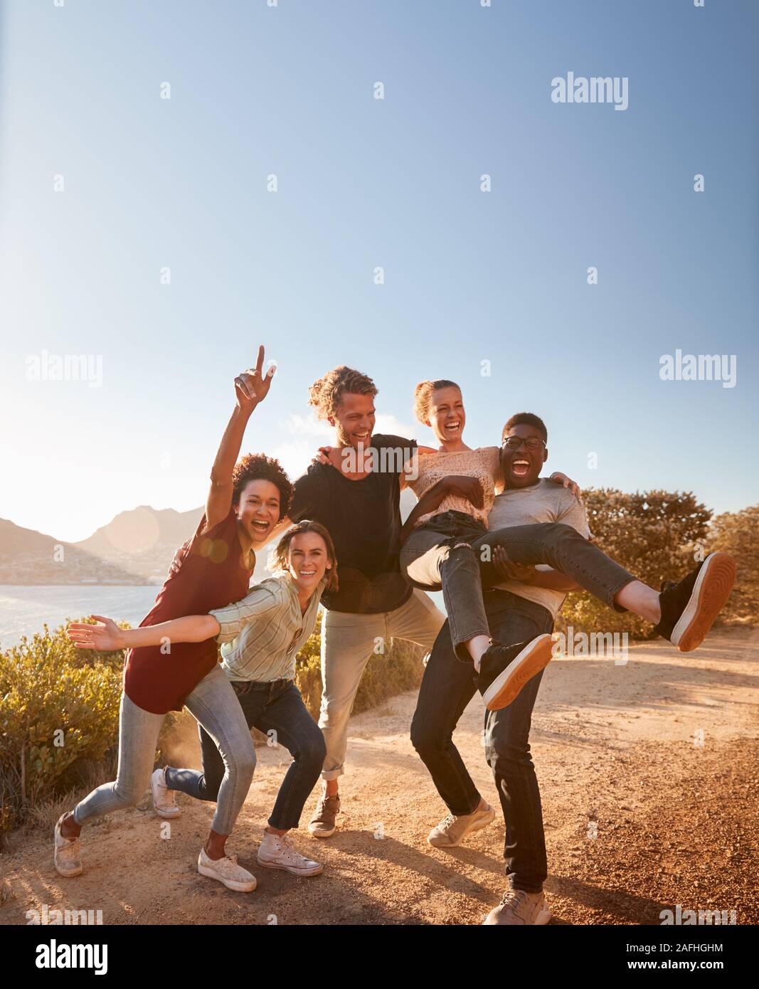 Cinque amici millenario in un viaggio su strada hanno divertimento che posano per una foto su un sentiero costiero a piena lunghezza Foto Stock