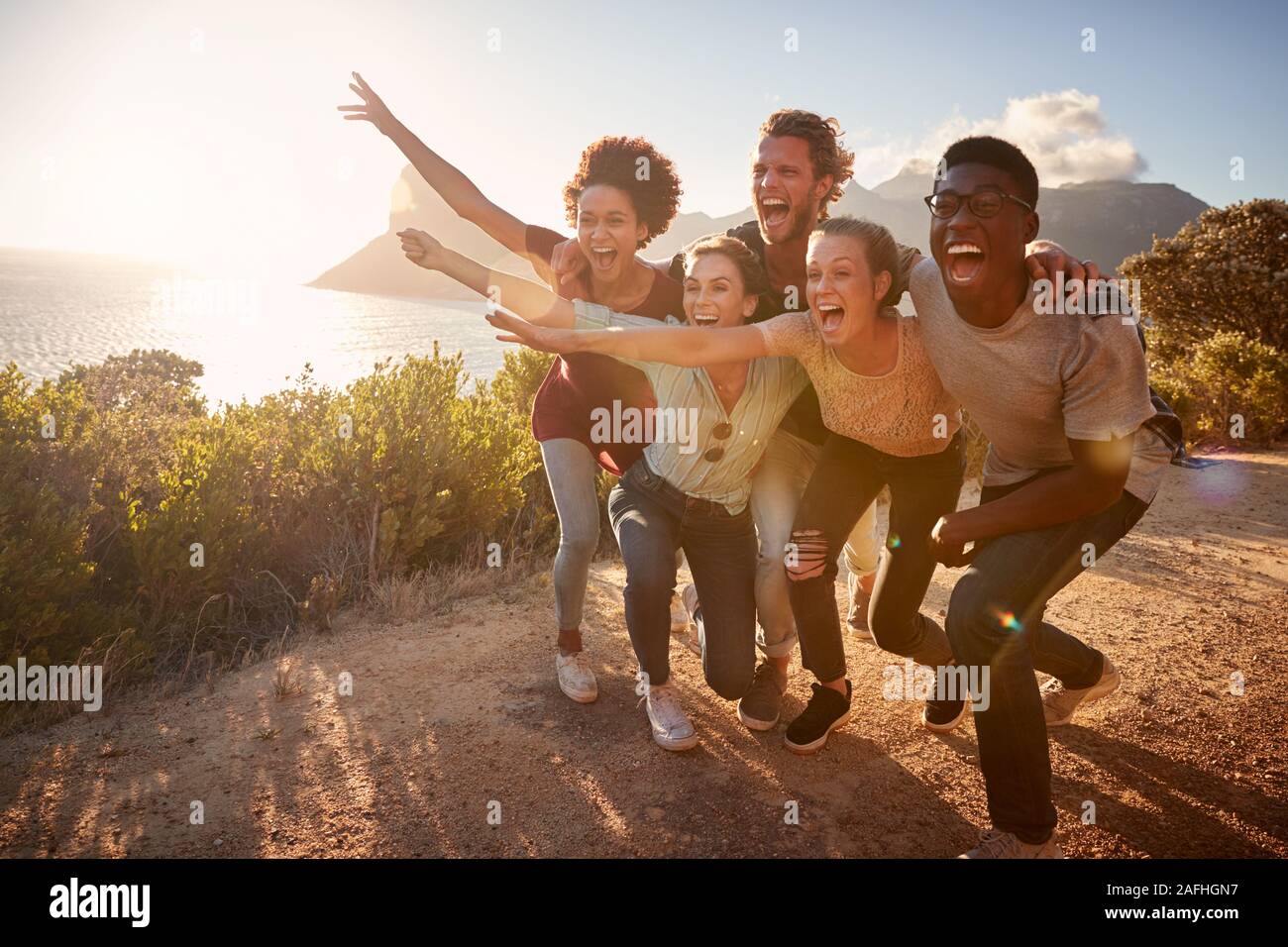 Cinque amici millenario in un viaggio su strada hanno divertimento che posano per una foto su un sentiero costiero a piena lunghezza Foto Stock