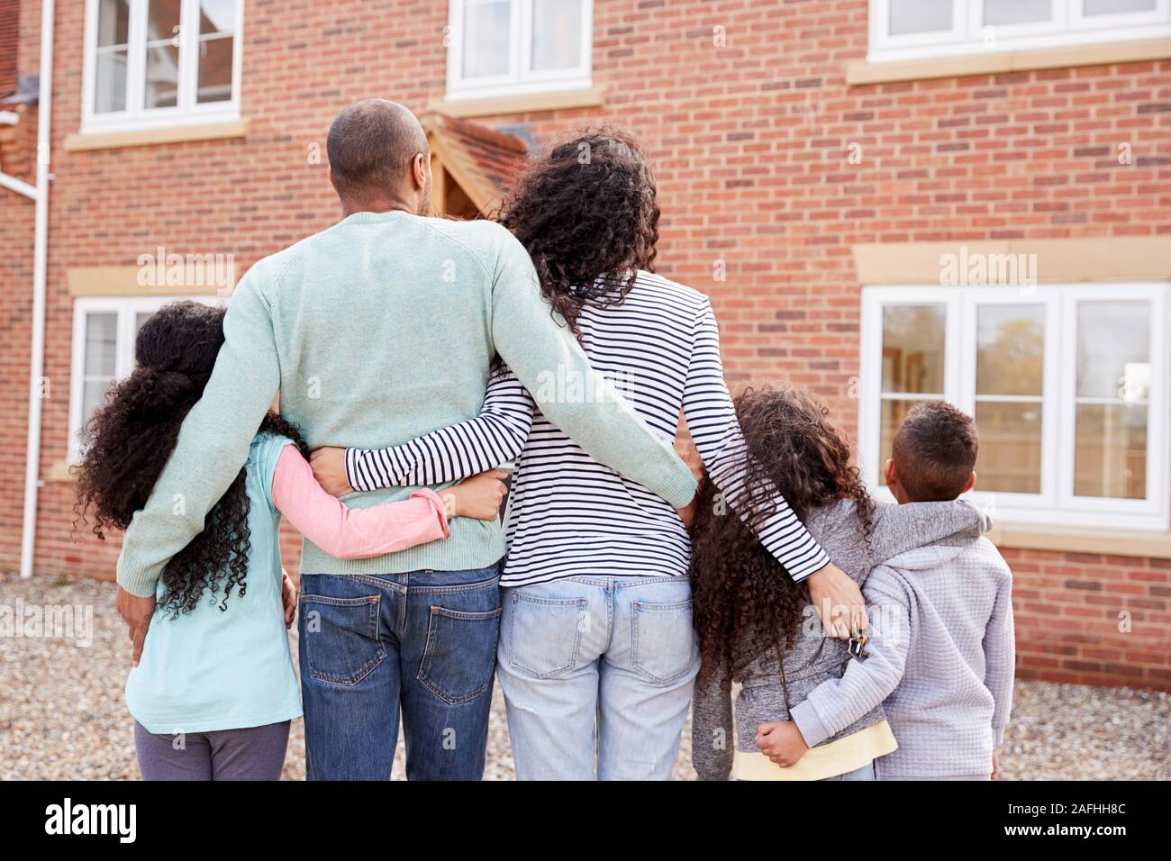 Vista posteriore della famiglia in piedi al di fuori di nuovo Home sullo spostamento di giorno a guardare House Foto Stock