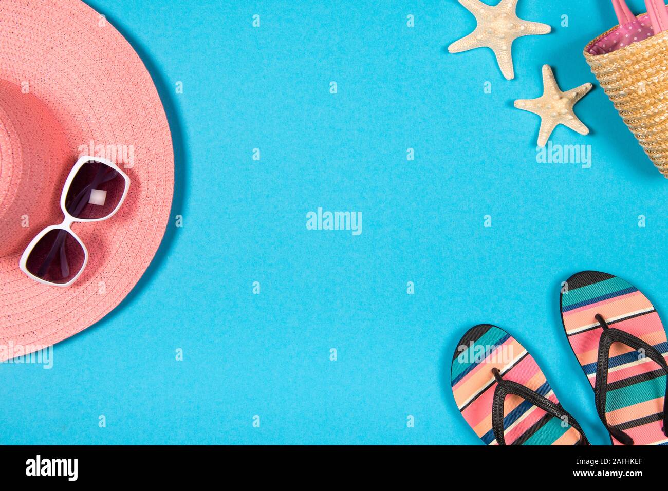 Laici piatta con una vacanza estiva concetto con sfondo blu un cappello rosa, occhiali da sole, flip-flop e spiaggia accessoires visto da un angolo alto Foto Stock