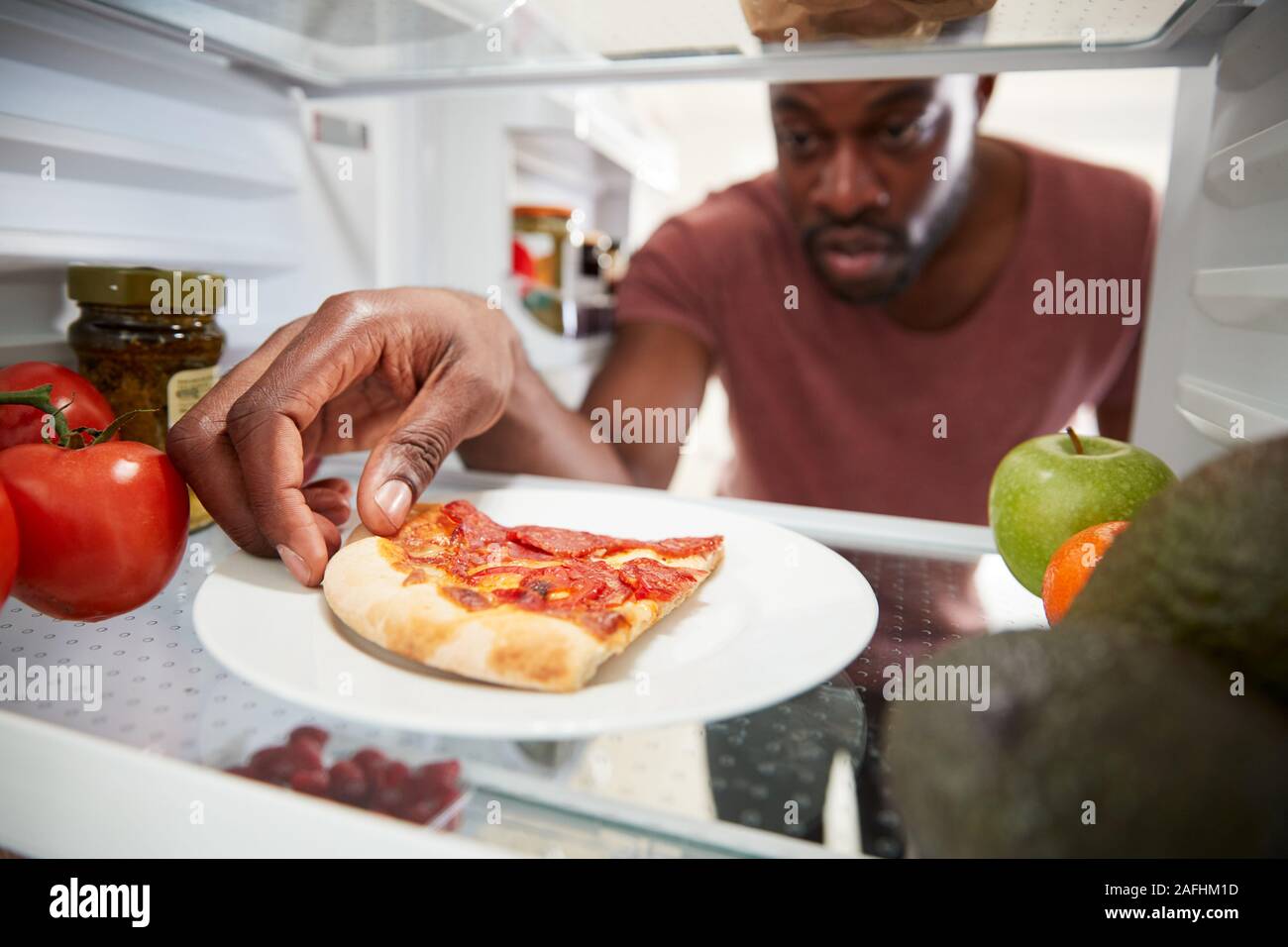 Vista dall'interno del frigorifero come uomo apre la porta per eventuali avanzi di pizza da asporto Slice Foto Stock