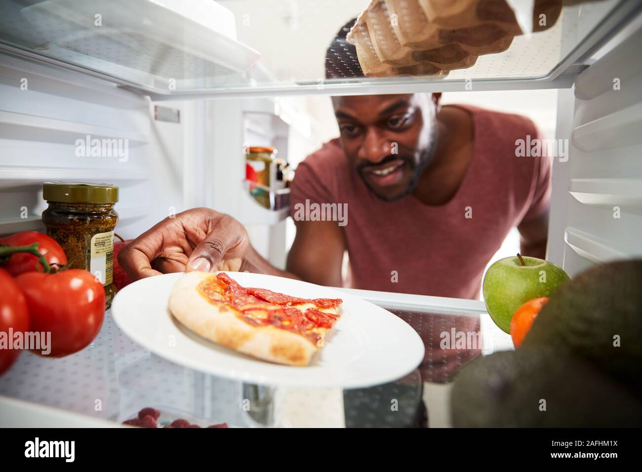 Vista dall'interno del frigorifero come uomo apre la porta per eventuali avanzi di pizza da asporto Slice Foto Stock