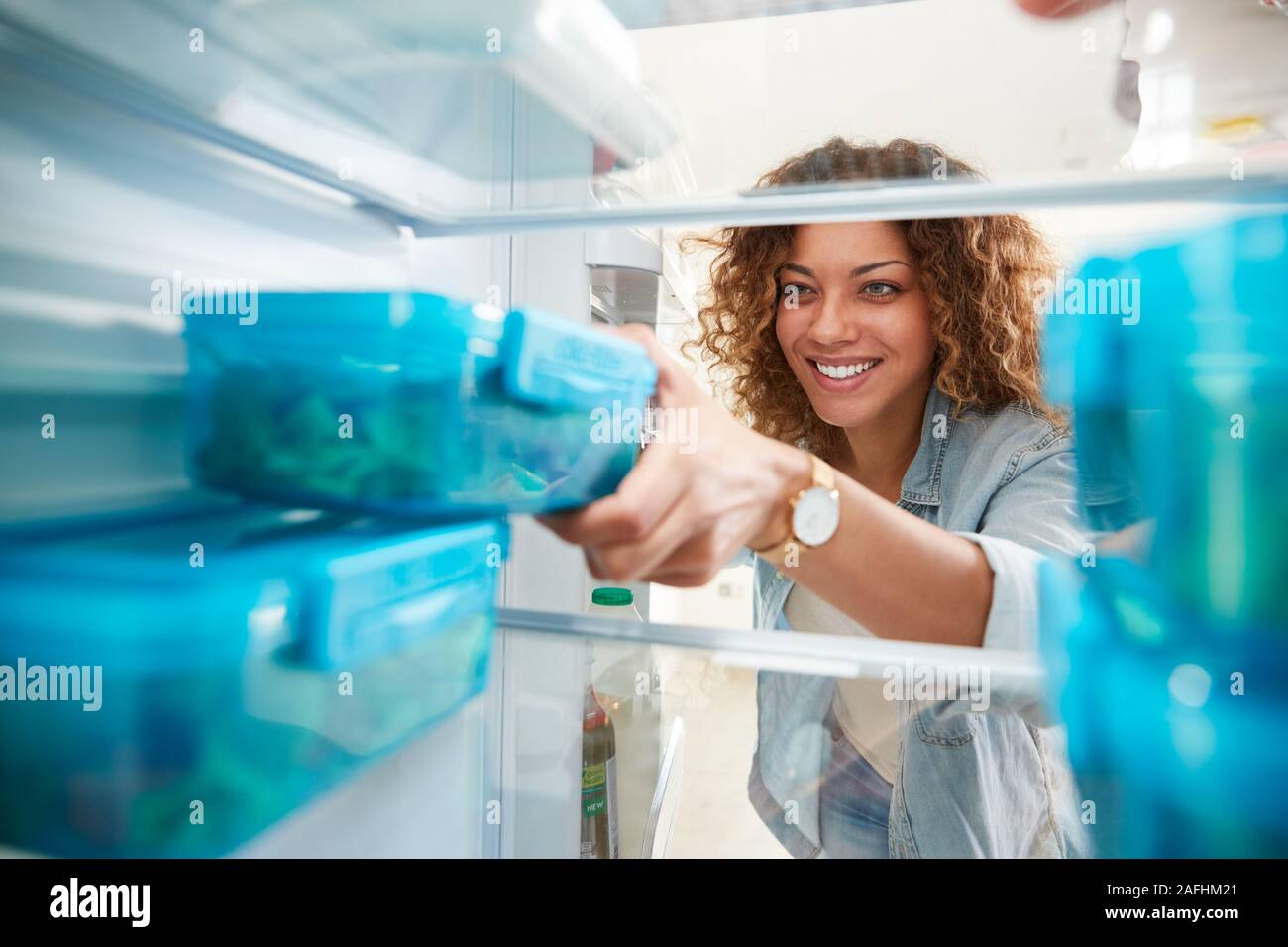 Vista dall'interno del frigorifero come donna toglie fuori una sana il pranzo al sacco nel contenitore Foto Stock