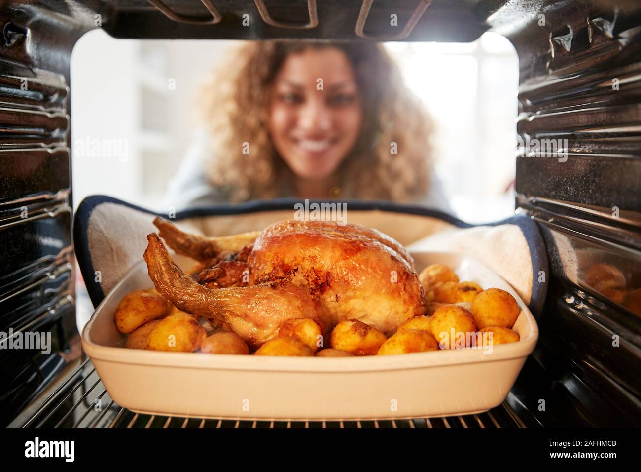 Vista guardando fuori dall'interno del forno come donna cuochi domenica pollo arrosto cena Foto Stock